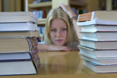 Deutschland, Baden-Württemberg, gestresste junge Studentin mit Bücherstapel in einer Bibliothek - CHAF000106