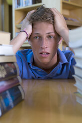 Deutschland, Baden-Württemberg, gestresster junger Student mit Bücherstapel in einer Bibliothek - CHAF000107