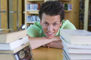 Deutschland, Baden-Württemberg, glücklicher junger Student mit Bücherstapel in einer Bibliothek - CHAF000101