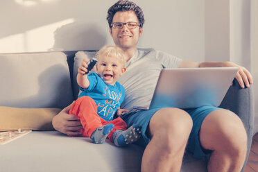 Father and son sitting on the couch with laptop - MFF000836