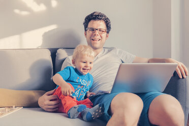 Father and son sitting on the couch with laptop - MFF000837