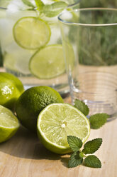 Sliced and whole limes and glass on wooden table - YFF000012