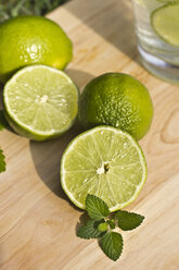 Sliced and whole limes and glass on wooden table - YFF000013