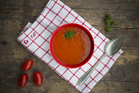 Schüssel mit Tomatensuppe auf Küchenhandtuch und Holztisch, lizenzfreies Stockfoto