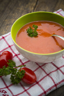 Bowl of tomato soup and tomatoes on kitchen towel and wooden table - LVF000509