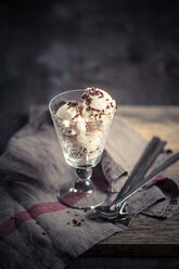 Glass of vanilla icecream with chocolate granules, spoons and kitchen towel on wood - SBDF000510