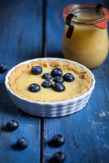 Zitronenkuchen mit Blaubeeren und Glas Zitronenquark auf blauem Holztisch - SBDF000493