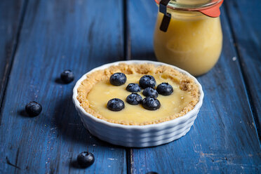 Zitronenkuchen mit Blaubeeren und Glas Zitronenquark auf blauem Holztisch - SBDF000526