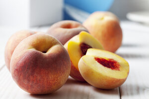 Whole and sliced peaches (Prunus persica) on white wooden table - CSF020783