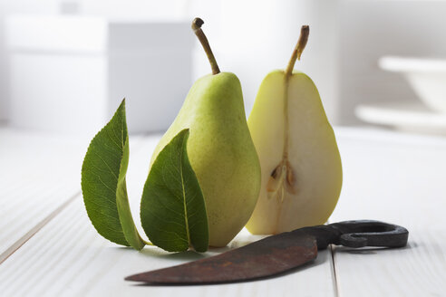 Zwei Hälften einer Birne (Pyrus), Blätter und rostiges Messer auf weißem Holztisch - CSF020789