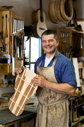 Lächelnder Gitarrenbauer in seiner Werkstatt - TC003853