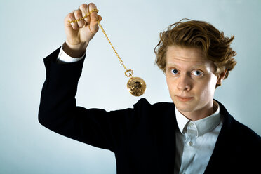 Portrait of young man swinging golden pocket watch - TCF003836