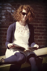 Junge Frau mit Sonnenbrille hält Zeitschrift - HOHF000417