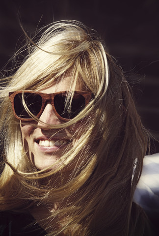 Lächelnde junge Frau mit wehenden Haaren und Sonnenbrille, lizenzfreies Stockfoto