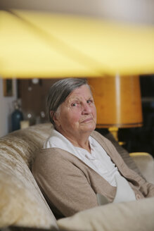 Ältere Frau sitzt auf einer Couch im Wohnzimmer - JATF000661