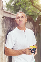 Älterer Mann lehnt mit einer Kaffeetasse in der Hand an einer Mauer im Hinterhof - MFF000852