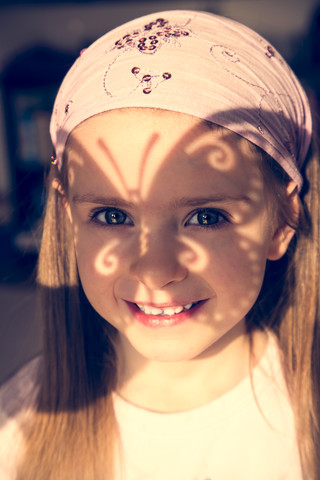 Porträt eines lächelnden kleinen Mädchens mit schmetterlingsförmigem Schatten auf ihrem Gesicht, lizenzfreies Stockfoto