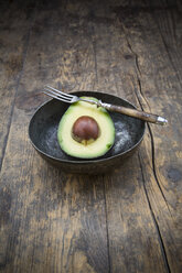 Bowl with half of avocado (Persea Americana) on wooden table - LVF000591