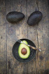 Zwei ganze und eine halbe Avocado (Persea Americana) auf einem Holztisch - LVF000592