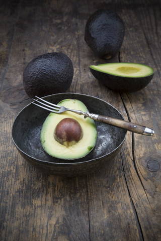 Geschnittene und ganze Avocados (Persea Americana) auf einem Holztisch, lizenzfreies Stockfoto