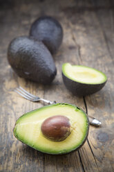 Sliced and whole avocados (Persea Americana) on wooden table - LVF000594