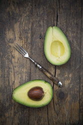 Two halves of an avocado (Persea Americana) and a fork on wooden table - LVF000595