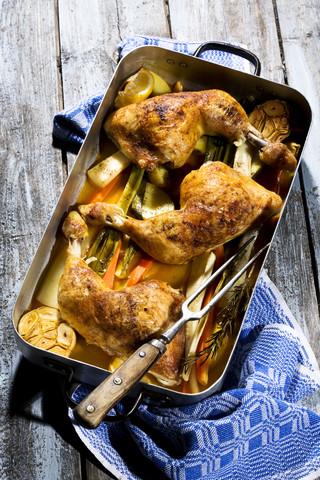 Bratentablett mit geschmorten Hähnchentrommeln, Kartoffeln, Karotten, Knoblauch, Frühlingszwiebeln, Petersilienwurzeln und Zitrone in Weißweinsauce, lizenzfreies Stockfoto