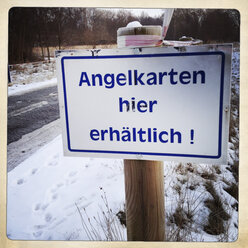 Schild für Angelkarten an verschneiter Straße, Brandenburg, Deutschland - ZMF000196