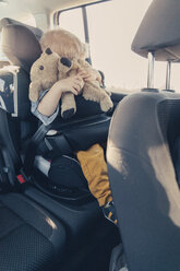 Germany, Little boy sitting in back-seat car seat, holding his stuffed animal - MFF000886