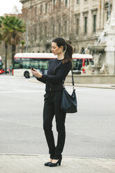 Spain, Catalunya, Barcelona, young black dressed businesswoman looking at her smartphone in front of a street - EBSF000004