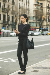 Spain, Catalunya, Barcelona, young black dressed businesswoman telephoning in front of a street - EBSF000005