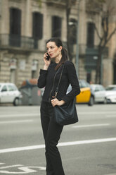 Spain, Catalunya, Barcelona, young black dressed businesswoman telephoning in front of a street - EBSF000007