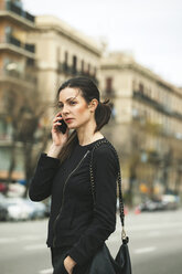 Spain, Catalunya, Barcelona, young black dressed businesswoman telephoning in front of a street - EBSF000009