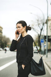 Spain, Catalunya, Barcelona, young black dressed businesswoman telephoning in front of a street - EBSF000010