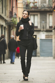 Spain, Catalunya, Barcelona, young black dressed businesswoman with coffee to go in front of a street - EBSF000012