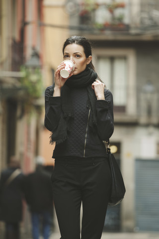 Spanien, Katalonien, Barcelona, junge schwarz gekleidete Geschäftsfrau trinkt Kaffee zum Mitnehmen vor einer Straße, lizenzfreies Stockfoto