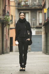 Spain, Catalunya, Barcelona, young black dressed businesswoman with coffee to go in front of a street - EBSF000014