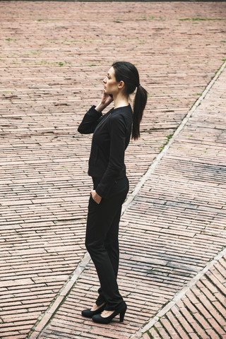 Spanien, Katalonien, Barcelona, junge schwarz gekleidete Geschäftsfrau beim Telefonieren auf einem Platz, lizenzfreies Stockfoto