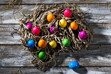 Easter nest of brown paper stripes with coloured Easter eggs on wood - MAEF007777