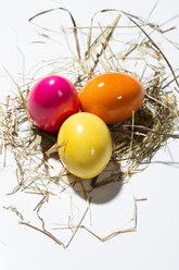 Three coloured Easter eggs and straw on white ground - MAEF007773