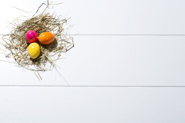 Three coloured Easter eggs and straw on white ground - MAEF007772
