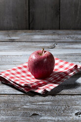 Roter Apfel auf Stoffserviette und Holztisch - MAEF007769