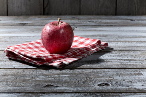 Roter Apfel auf Stoffserviette und Holztisch - MAEF007767