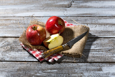 Sliced and whole red apples and a knife on jute, cloth napkin and wooden table - MAEF007765