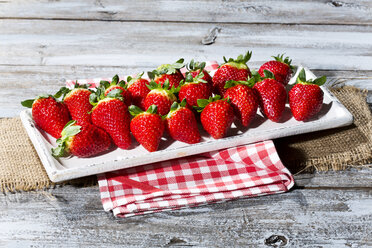 Teller mit Erdbeeren (Fragaria) auf Jute, Küchenhandtuch und Holztisch - MAEF007838