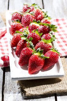 Teller mit Erdbeeren (Fragaria) auf Jute, Küchenhandtuch und Holztisch - MAEF007840