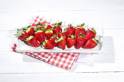 Teller mit Erdbeeren (Fragaria) auf Küchenhandtuch und weißem Holztisch - MAEF007843