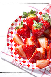 Teller mit geschnittenen und ganzen Erdbeeren (Fragaria) auf einem Küchenhandtuch, Nahaufnahme - MAEF007846