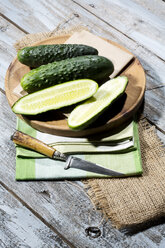 Sliced and whole cucumbers (Cucumis sativus) with knife on chopping board - MAEF007823