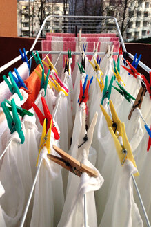 clothes drying rack with mostly white clothes and colorful pegs on a balcony - NKF000060